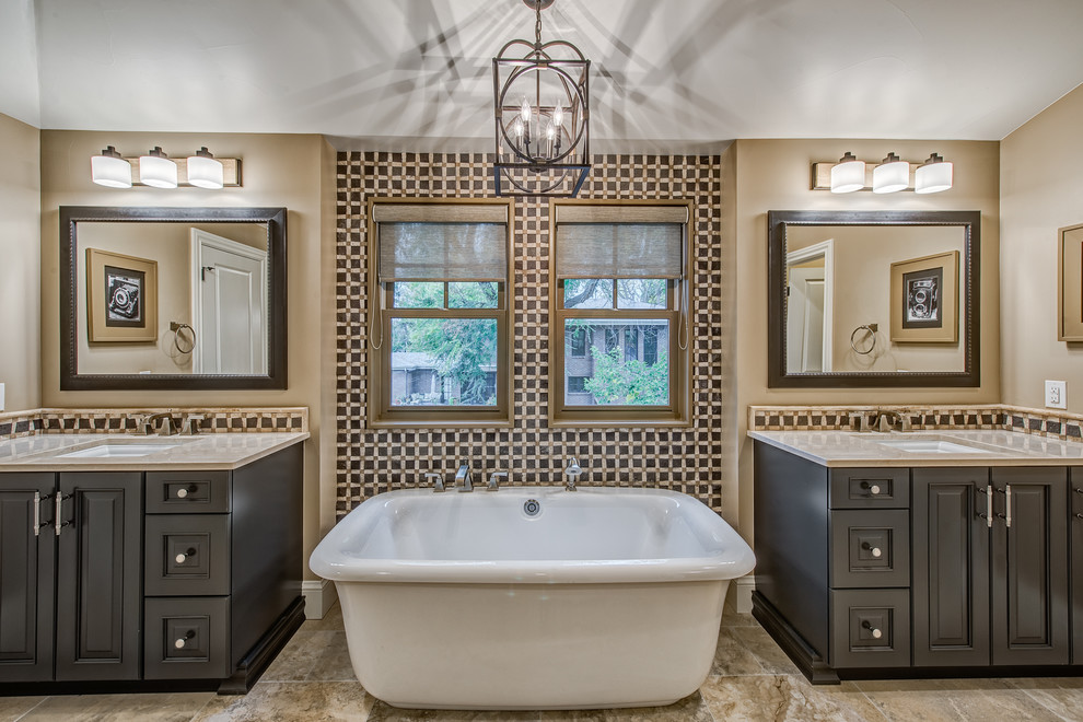 This is an example of a traditional bathroom in Denver with raised-panel cabinets, a freestanding tub, ceramic tile, beige walls, porcelain floors, an undermount sink and dark wood cabinets.