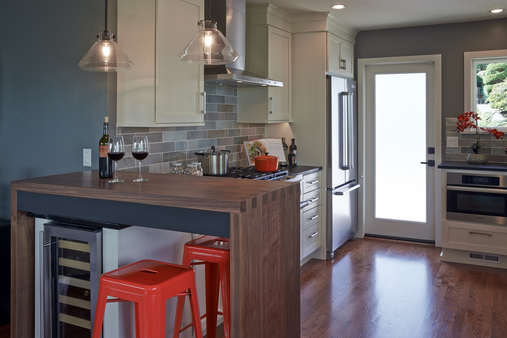 Photo of a transitional galley eat-in kitchen in Seattle with an undermount sink, shaker cabinets, white cabinets, grey splashback, slate splashback, stainless steel appliances and brown floor.