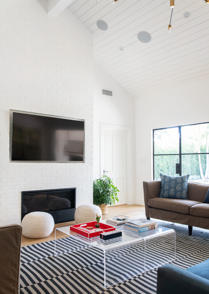 This is an example of a large transitional formal open concept living room in Los Angeles with white walls, medium hardwood floors, a standard fireplace, a brick fireplace surround, a wall-mounted tv and brown floor.