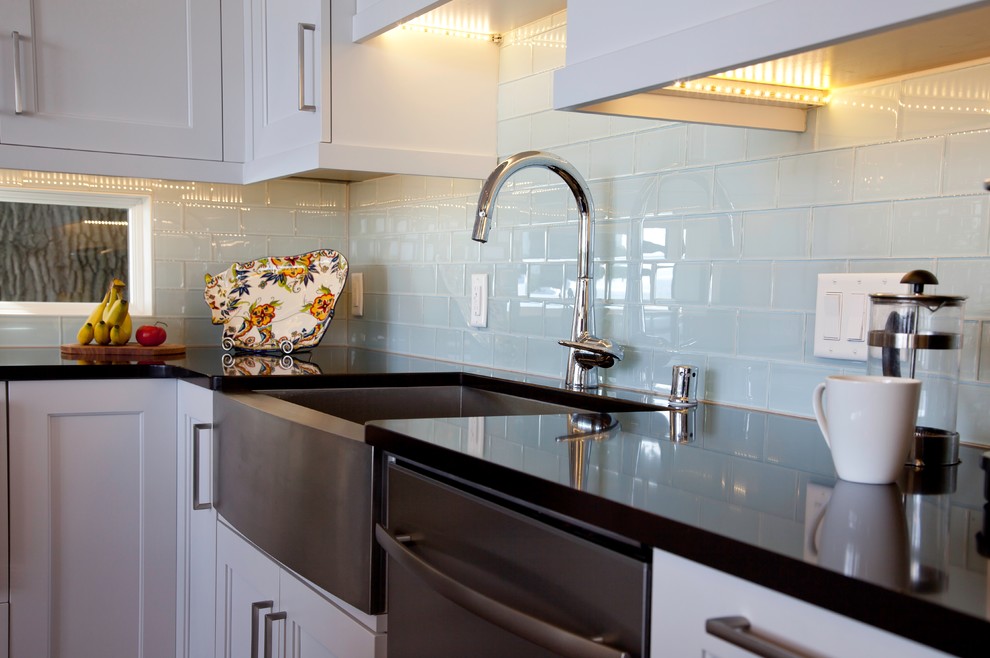 Eat-in kitchen - large transitional l-shaped medium tone wood floor and brown floor eat-in kitchen idea with a farmhouse sink, shaker cabinets, white cabinets, quartzite countertops, blue backsplash, glass sheet backsplash, stainless steel appliances and an island