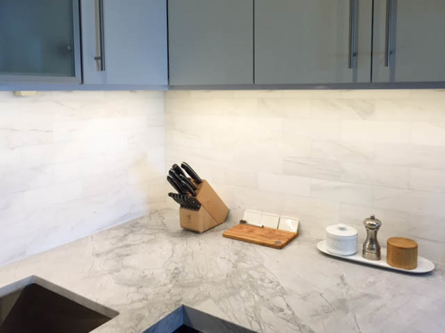 This is an example of a small contemporary u-shaped kitchen in New York with an undermount sink, flat-panel cabinets, grey cabinets, quartzite benchtops, white splashback, stone tile splashback and stainless steel appliances.