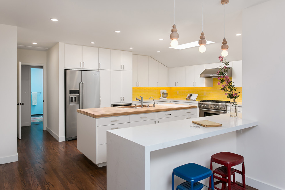 Photo of a mid-sized midcentury u-shaped eat-in kitchen in Los Angeles with a double-bowl sink, flat-panel cabinets, white cabinets, wood benchtops, yellow splashback, ceramic splashback, stainless steel appliances, medium hardwood floors, with island and brown floor.