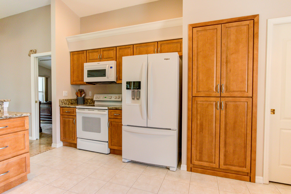 Example of a mid-sized kitchen design with an undermount sink, raised-panel cabinets, medium tone wood cabinets, granite countertops, white appliances and brown countertops