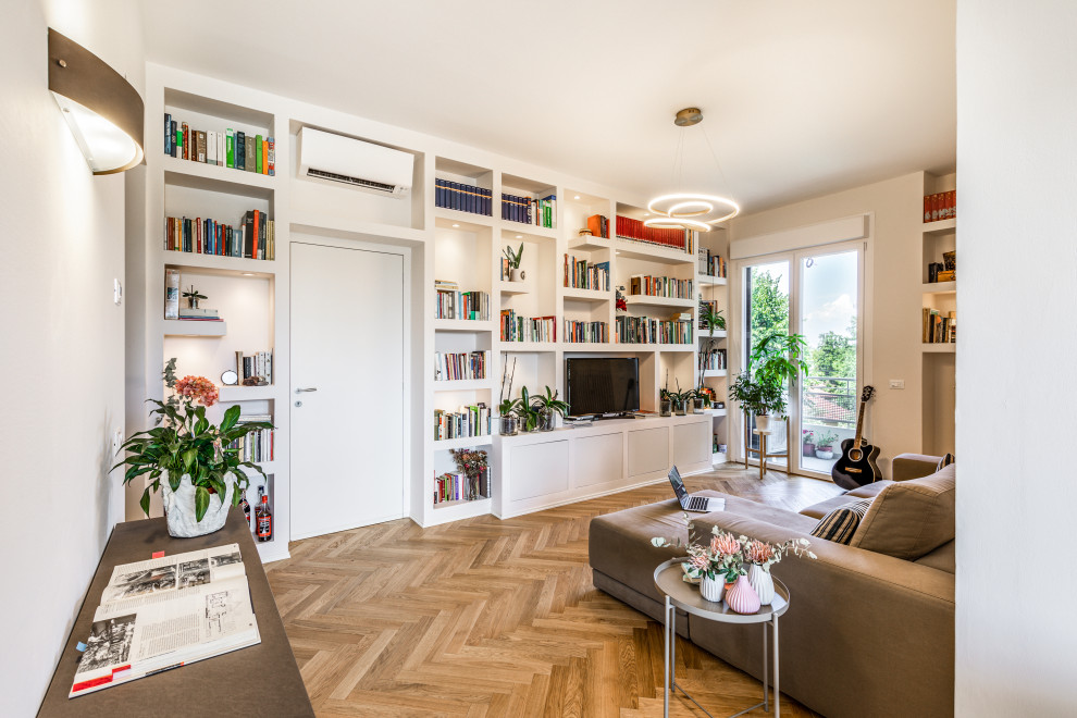 Esempio di un piccolo soggiorno minimalista aperto con libreria, pareti bianche, parquet chiaro, parete attrezzata e pavimento marrone