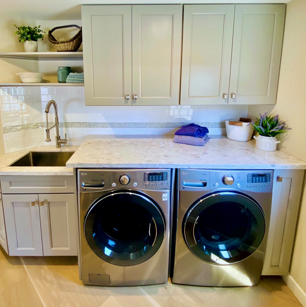 サンフランシスコにある低価格の中くらいなトランジショナルスタイルのおしゃれな洗濯室 (アンダーカウンターシンク、シェーカースタイル扉のキャビネット、グレーのキャビネット、クオーツストーンカウンター、白いキッチンパネル、ガラスタイルのキッチンパネル、ベージュの壁、淡色無垢フローリング、左右配置の洗濯機・乾燥機、白いキッチンカウンター) の写真