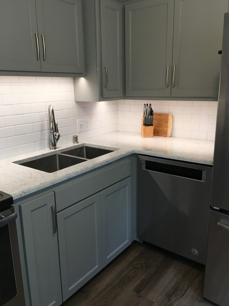 Mid-sized transitional l-shaped vinyl floor eat-in kitchen photo with an undermount sink, shaker cabinets, quartz countertops, white backsplash and stainless steel appliances