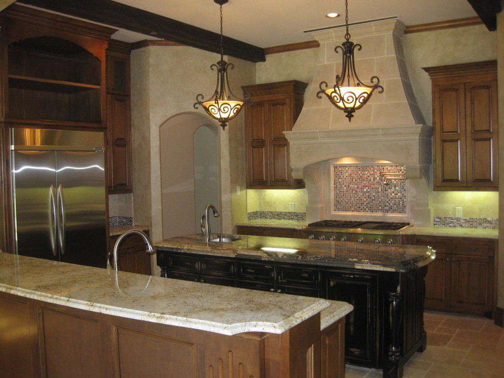This is an example of a large traditional u-shaped eat-in kitchen in Dallas with a single-bowl sink, raised-panel cabinets, medium wood cabinets, granite benchtops, beige splashback, stone tile splashback, stainless steel appliances, travertine floors and multiple islands.