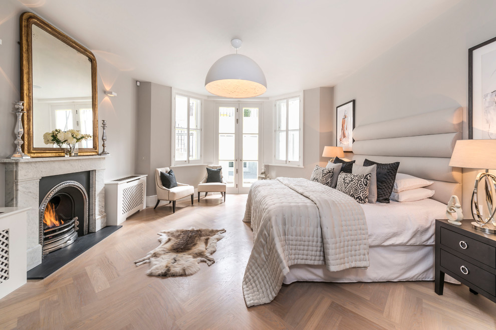 Inspiration for a transitional bedroom in London with beige walls, light hardwood floors, a standard fireplace and beige floor.