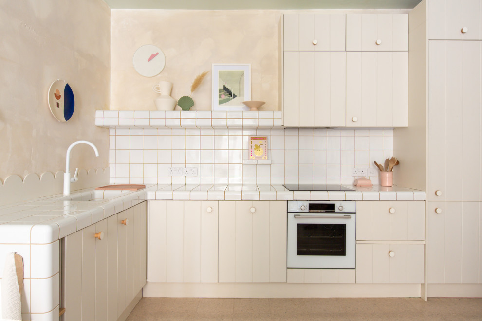 Inspiration for a bohemian open plan kitchen in Kent with beaded cabinets, beige cabinets, tile countertops, white splashback, ceramic splashback, cork flooring, beige floors and white worktops.