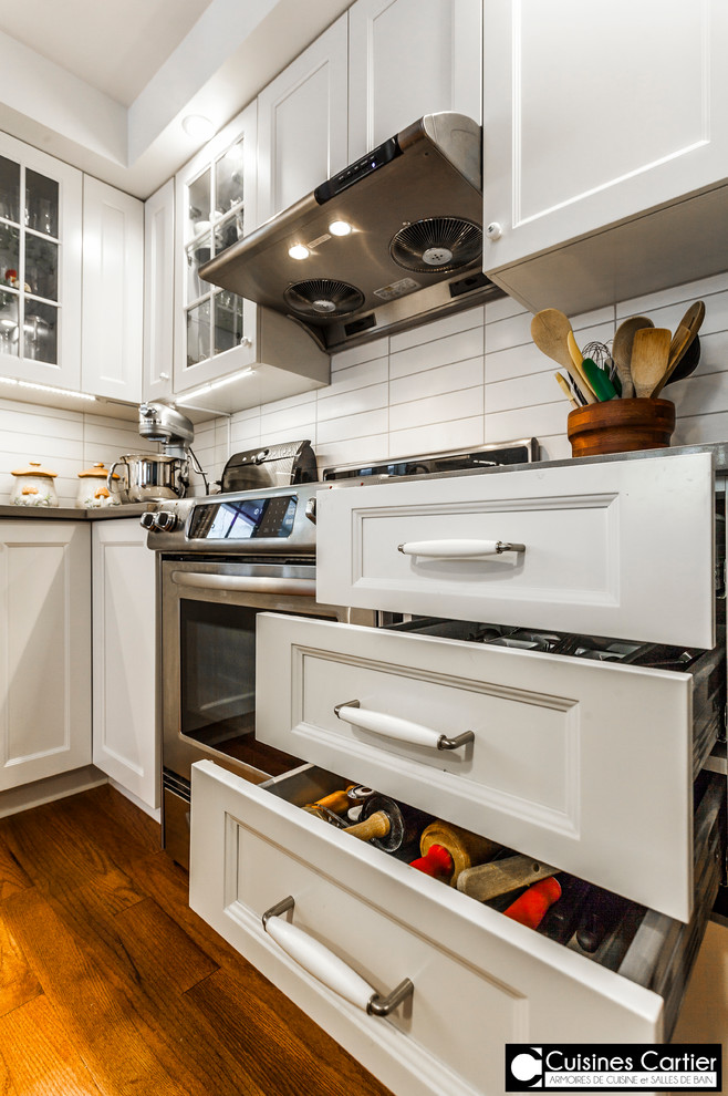 Example of a large transitional medium tone wood floor eat-in kitchen design in Montreal with a double-bowl sink, shaker cabinets, white cabinets, quartzite countertops, white backsplash, ceramic backsplash, stainless steel appliances and an island