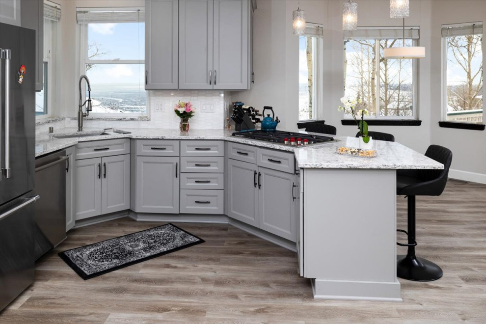 Example of a mid-sized transitional laminate floor and gray floor open concept kitchen design with recessed-panel cabinets, gray cabinets, quartz countertops, white backsplash, marble backsplash, stainless steel appliances and white countertops