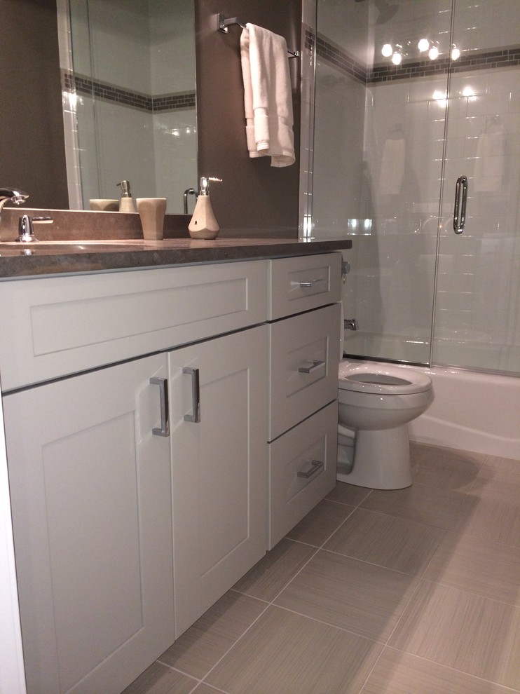 Photo of a mid-sized contemporary kids bathroom in Chicago with an undermount sink, recessed-panel cabinets, grey cabinets, limestone benchtops, a one-piece toilet, gray tile, porcelain tile, brown walls and porcelain floors.