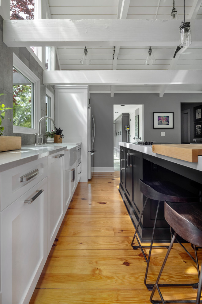 Mid-sized minimalist galley light wood floor, brown floor and exposed beam eat-in kitchen photo in Detroit with an undermount sink, recessed-panel cabinets, white cabinets, quartz countertops, gray backsplash, porcelain backsplash, stainless steel appliances, an island and white countertops