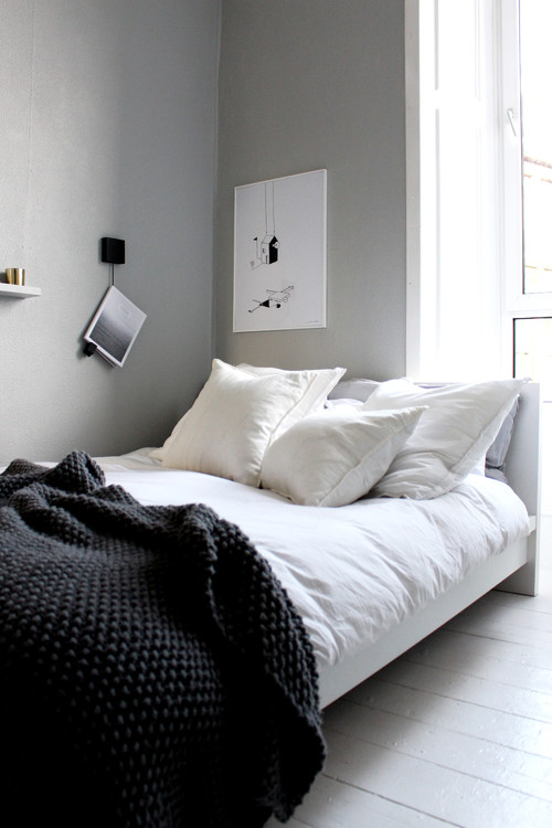 Soveværelse med lyse grå vægge og hvide gulve. Meget rent og lækkert med grafisk sort/hvid kunst på væggen, hvidt sengetøj og et mørkt sengetæppe