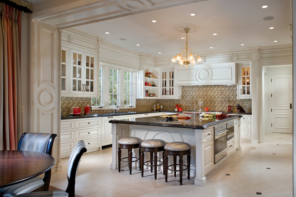 Photo of a large traditional l-shaped eat-in kitchen in Orange County with white cabinets, granite benchtops, multi-coloured splashback, stainless steel appliances, limestone floors, with island, an undermount sink, raised-panel cabinets, ceramic splashback and beige floor.