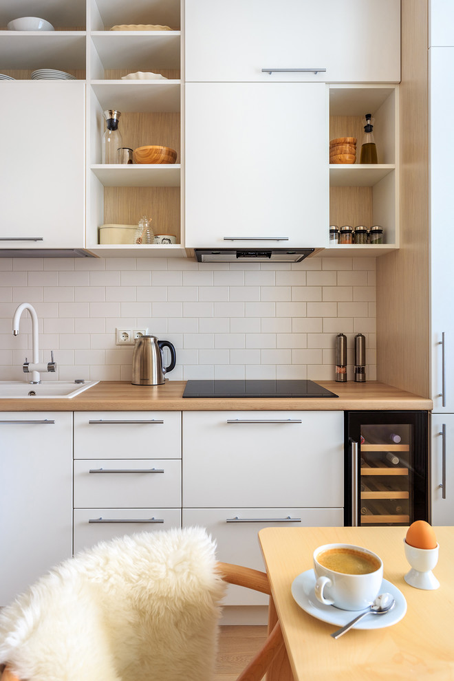 Photo of a small scandinavian l-shaped separate kitchen in Moscow with a drop-in sink, flat-panel cabinets, white cabinets, laminate benchtops, white splashback, ceramic splashback, stainless steel appliances, light hardwood floors and beige floor.