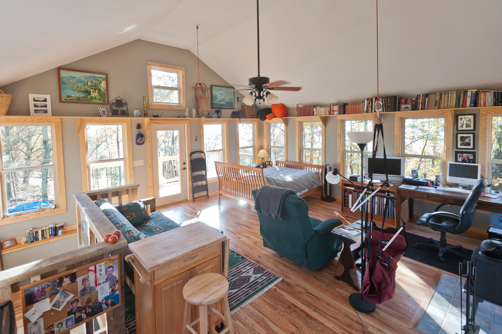 This is an example of a small arts and crafts loft-style living room in Atlanta with grey walls, a wood stove, a tile fireplace surround, a library, medium hardwood floors, a freestanding tv and brown floor.