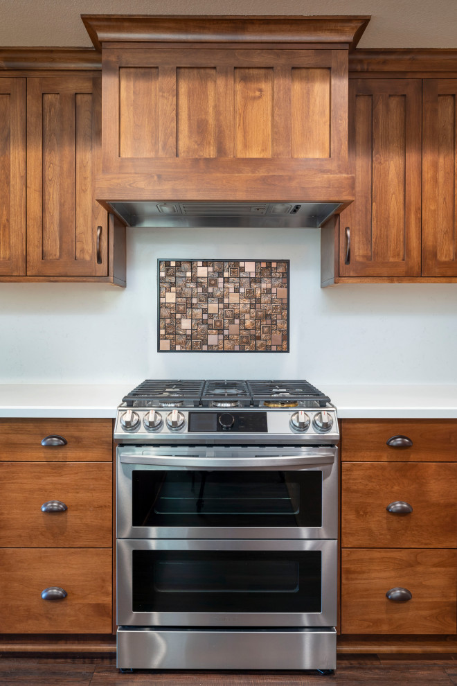 Exempel på ett stort amerikanskt flerfärgad flerfärgat u-kök, med en trippel diskho, luckor med upphöjd panel, skåp i mellenmörkt trä, bänkskiva i kvarts, vitt stänkskydd, rostfria vitvaror, vinylgolv, en köksö och brunt golv