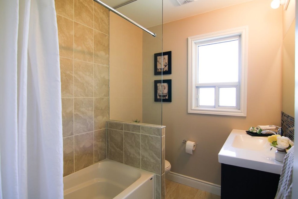 Photo of a small transitional 3/4 bathroom in Toronto with dark wood cabinets, an alcove tub, a shower/bathtub combo, a two-piece toilet, multi-coloured tile, matchstick tile, beige walls, vinyl floors, an integrated sink and engineered quartz benchtops.