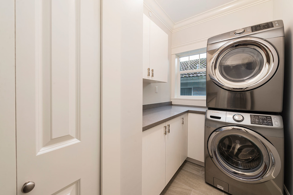 This is an example of a small transitional single-wall dedicated laundry room in Vancouver with flat-panel cabinets, white cabinets, laminate benchtops, white walls, porcelain floors and a stacked washer and dryer.