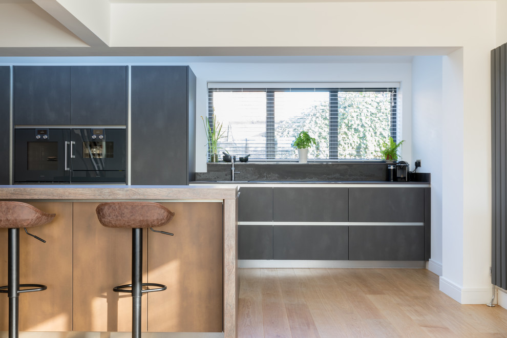 This is an example of a mid-sized industrial galley open plan kitchen in Sussex with an integrated sink, flat-panel cabinets, grey cabinets, tile benchtops, coloured appliances, with island and grey benchtop.