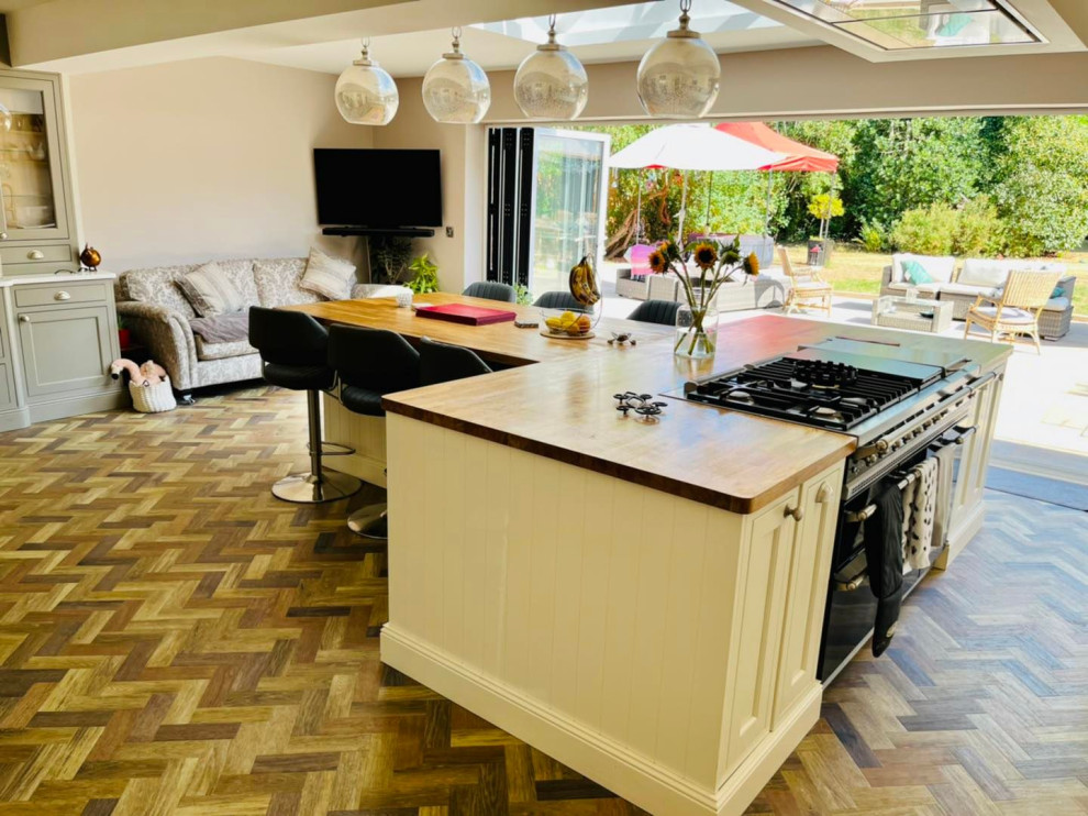 Inspiration for an expansive traditional kitchen in Buckinghamshire with a farmhouse sink, shaker cabinets, white cabinets, wood benchtops, white splashback, engineered quartz splashback, black appliances, vinyl floors, with island, brown floor, white benchtop and recessed.
