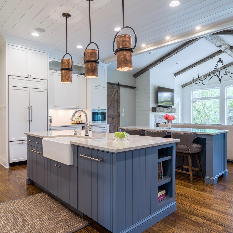 Large transitional l-shaped medium tone wood floor eat-in kitchen photo in Atlanta with a farmhouse sink, shaker cabinets, white cabinets, quartzite countertops, white backsplash, white appliances and two islands