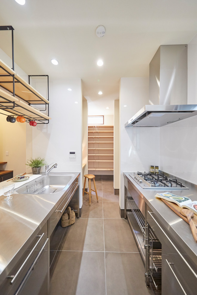 Industrial kitchen in Tokyo Suburbs with an integrated sink, flat-panel cabinets, stainless steel cabinets, stainless steel benchtops, a peninsula, grey floor and white benchtop.
