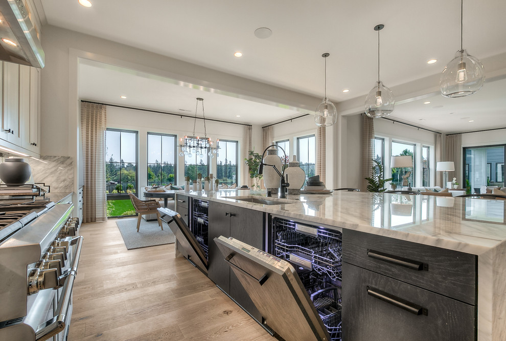 This is an example of an expansive transitional l-shaped open plan kitchen in Seattle with an undermount sink, recessed-panel cabinets, white cabinets, stainless steel appliances, light hardwood floors, with island and grey benchtop.