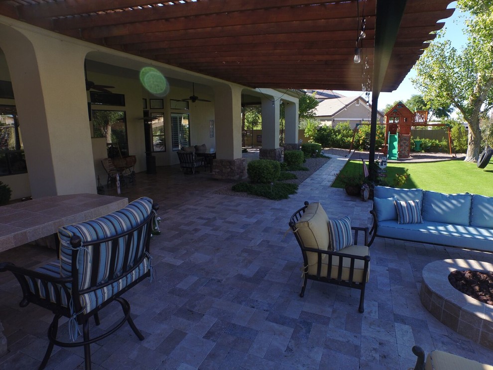 This is an example of a large traditional backyard patio in Phoenix with a fire feature, natural stone pavers and a roof extension.