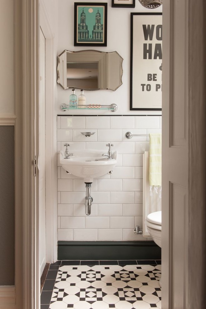 This is an example of a small traditional powder room in London with a wall-mount sink, black tile, white tile, subway tile, porcelain floors and white walls.
