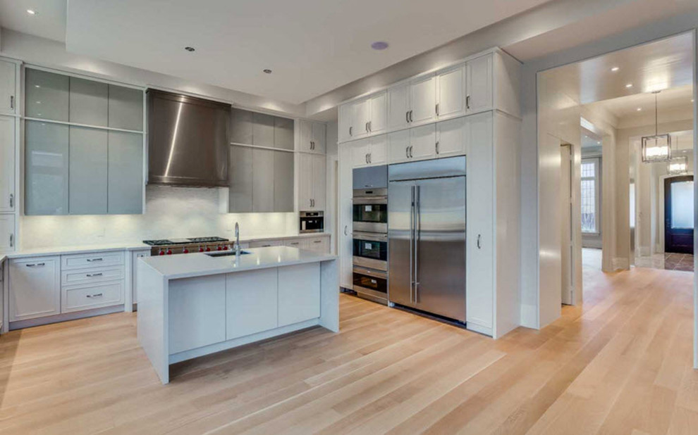 Example of a large transitional u-shaped light wood floor and brown floor kitchen design in Toronto with an undermount sink, beaded inset cabinets, white cabinets, quartz countertops, white backsplash, marble backsplash, stainless steel appliances and an island