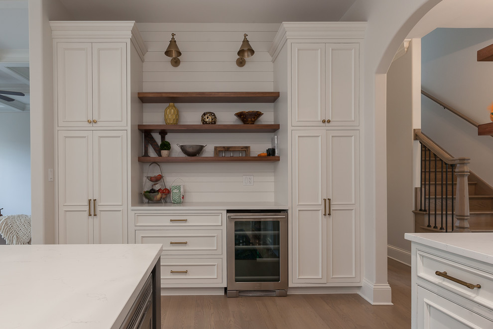 Design ideas for an expansive transitional u-shaped eat-in kitchen in Chicago with a farmhouse sink, beaded inset cabinets, white cabinets, quartz benchtops, white splashback, ceramic splashback, stainless steel appliances, medium hardwood floors, with island, grey floor and white benchtop.