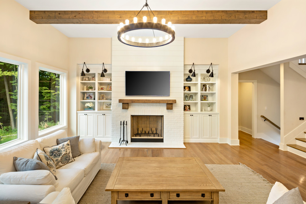 Inspiration for a transitional living room in Cincinnati with beige walls, medium hardwood floors, a standard fireplace, a brick fireplace surround, a wall-mounted tv and brown floor.