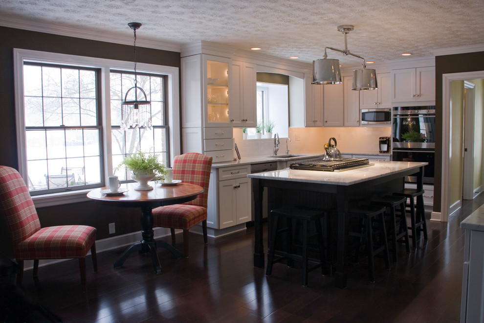 Large transitional l-shaped dark wood floor kitchen photo with shaker cabinets, white cabinets, marble countertops, white backsplash, stainless steel appliances and an island