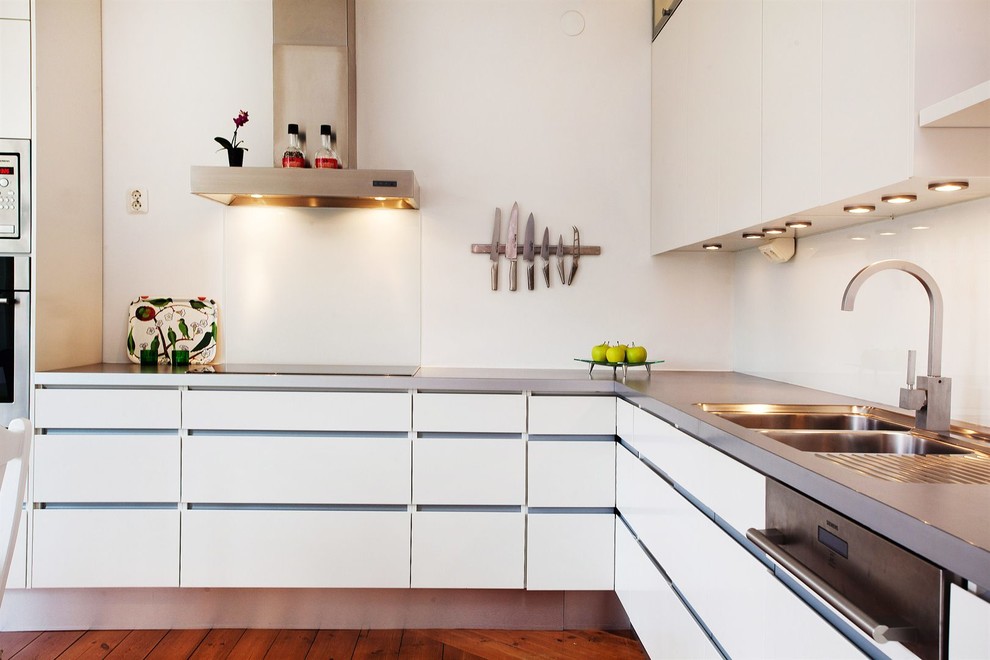Inspiration for a mid-sized scandinavian l-shaped separate kitchen in Stockholm with a double-bowl sink, flat-panel cabinets, white cabinets, stainless steel appliances, medium hardwood floors, no island and stainless steel benchtops.