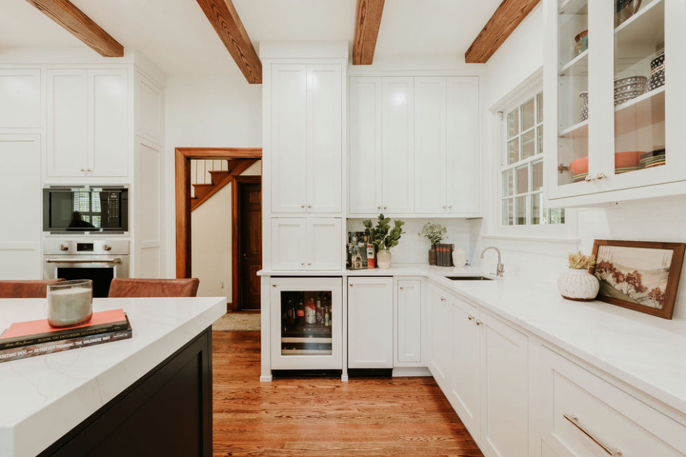 Large transitional u-shaped medium tone wood floor, brown floor and exposed beam eat-in kitchen photo with a single-bowl sink, recessed-panel cabinets, white cabinets, quartz countertops, white backsplash, marble backsplash, stainless steel appliances, an island and white countertops