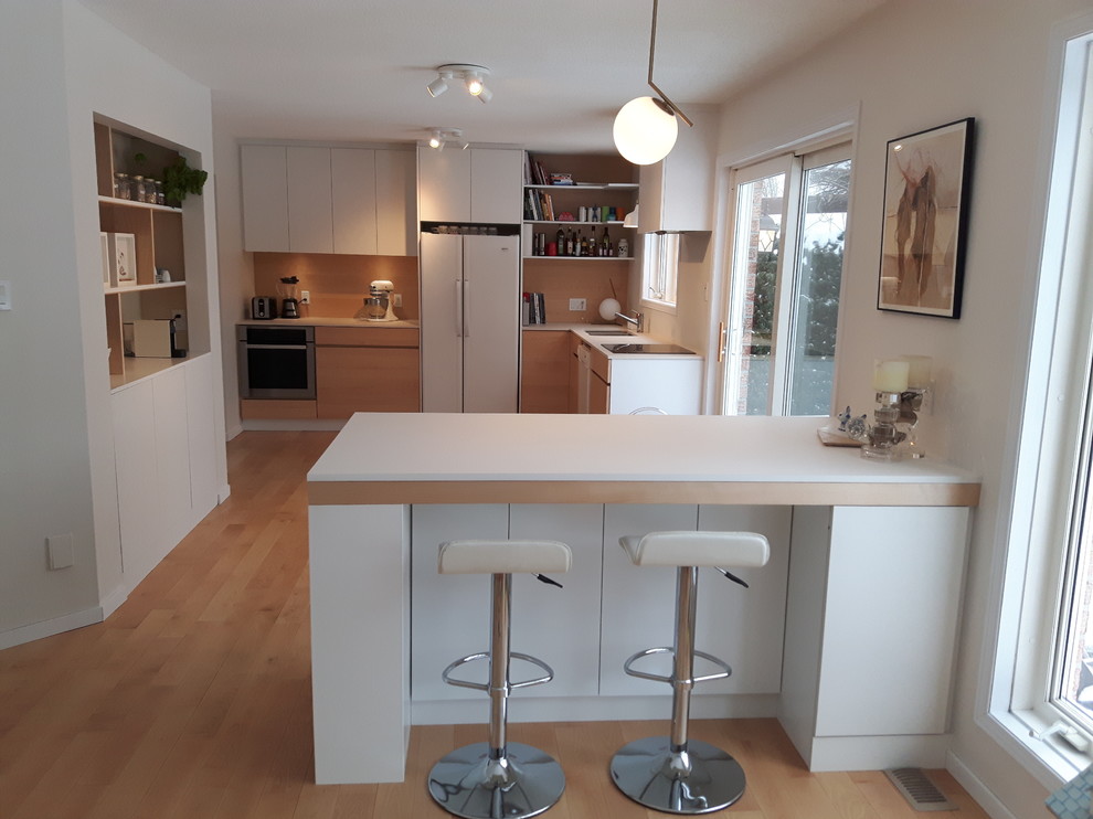 Photo of a small modern l-shaped separate kitchen in Ottawa with an undermount sink, flat-panel cabinets, white cabinets, solid surface benchtops, white appliances, light hardwood floors, with island and beige floor.
