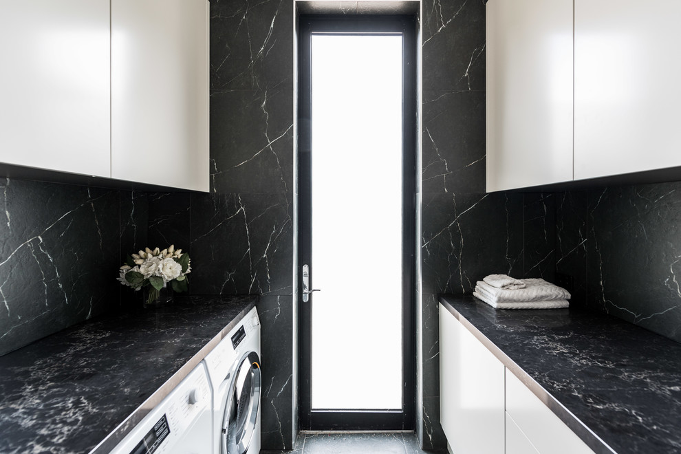 Design ideas for a large contemporary galley dedicated laundry room in Melbourne with a drop-in sink, flat-panel cabinets, beige cabinets, quartz benchtops, black walls, porcelain floors, a side-by-side washer and dryer and black floor.