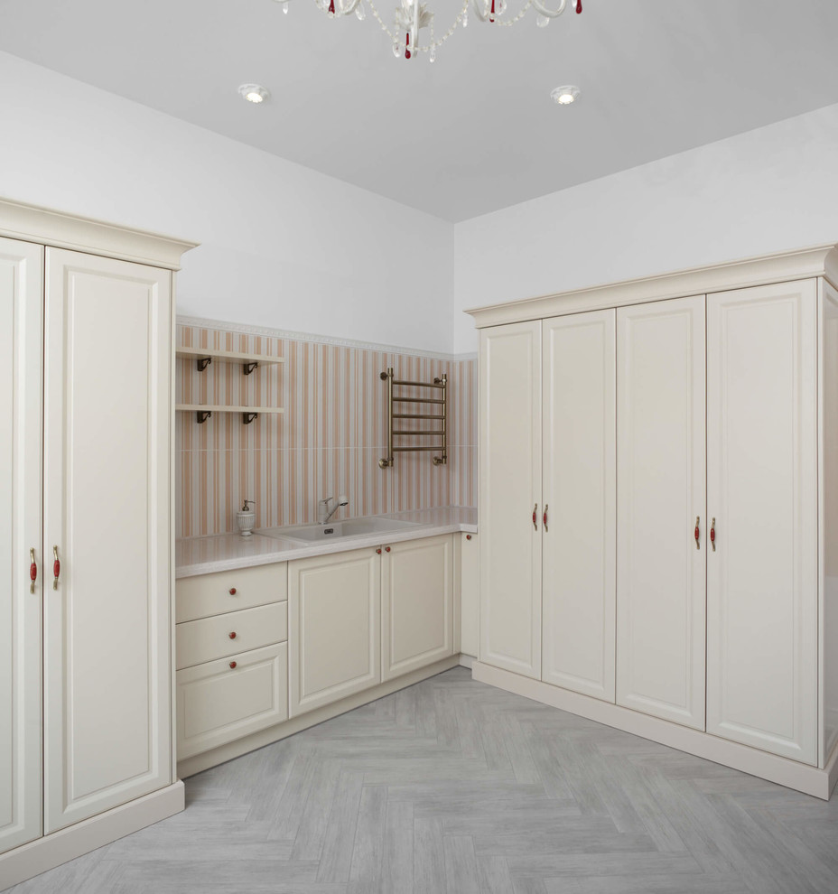 Photo of a large traditional l-shaped dedicated laundry room in Cleveland with a drop-in sink, raised-panel cabinets, laminate benchtops, white walls, beige cabinets, laminate floors and grey floor.