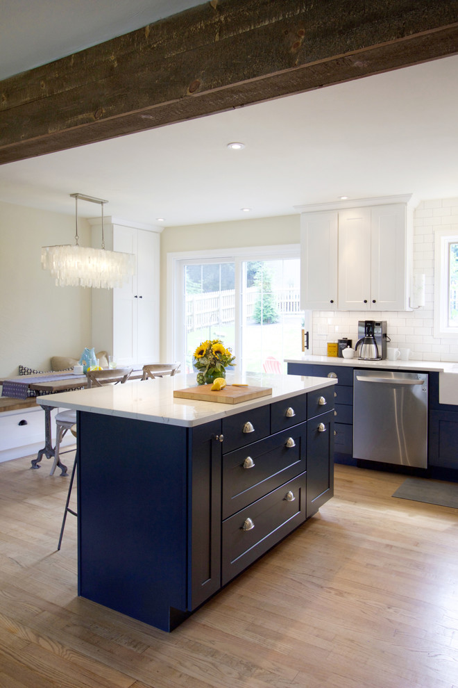 This is an example of a transitional eat-in kitchen in Other with a farmhouse sink, shaker cabinets, blue cabinets, quartz benchtops, white splashback, subway tile splashback, stainless steel appliances, medium hardwood floors, with island and white benchtop.