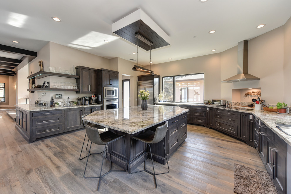 This is an example of a country u-shaped kitchen in Other with shaker cabinets, dark wood cabinets, stainless steel appliances, dark hardwood floors, with island, brown floor and grey benchtop.