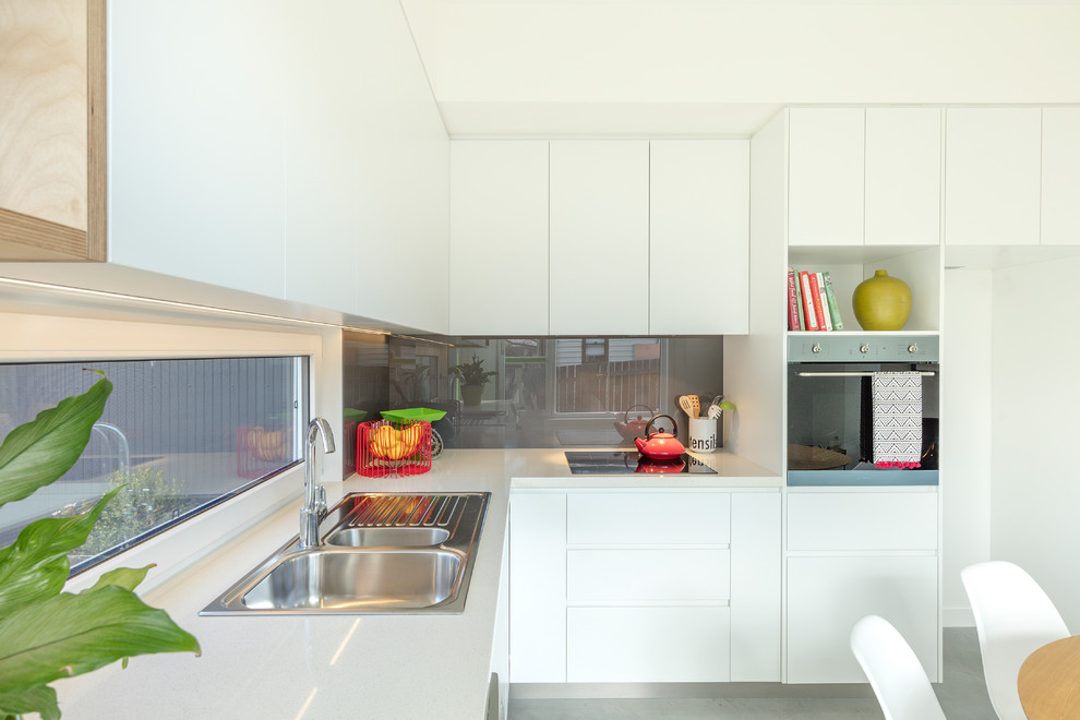 This is an example of a contemporary kitchen in Canberra - Queanbeyan with a double-bowl sink, flat-panel cabinets, white cabinets, quartz benchtops, grey splashback, glass sheet splashback, concrete floors, grey floor and white benchtop.