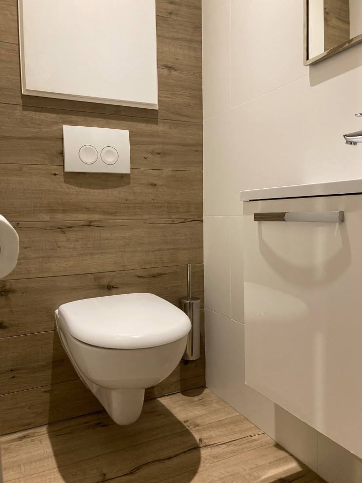 Cette image montre un petit WC suspendu nordique avec des portes de placard blanches, des carreaux de céramique, un mur blanc, un sol en carrelage imitation parquet, un lavabo suspendu et un sol beige.