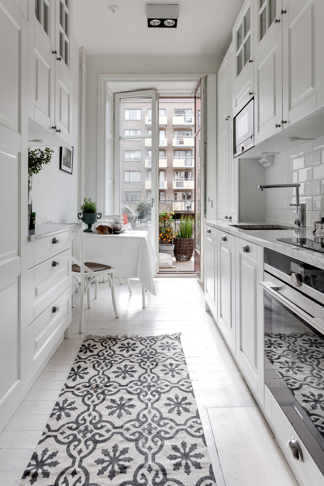 Mid-sized scandinavian galley eat-in kitchen in Stockholm with an undermount sink, raised-panel cabinets, white splashback, subway tile splashback, stainless steel appliances, painted wood floors and marble benchtops.