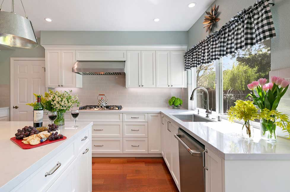 Photo of a mid-sized traditional l-shaped open plan kitchen in San Francisco with an undermount sink, recessed-panel cabinets, white cabinets, quartz benchtops, grey splashback, subway tile splashback, stainless steel appliances, medium hardwood floors, with island, brown floor and white benchtop.