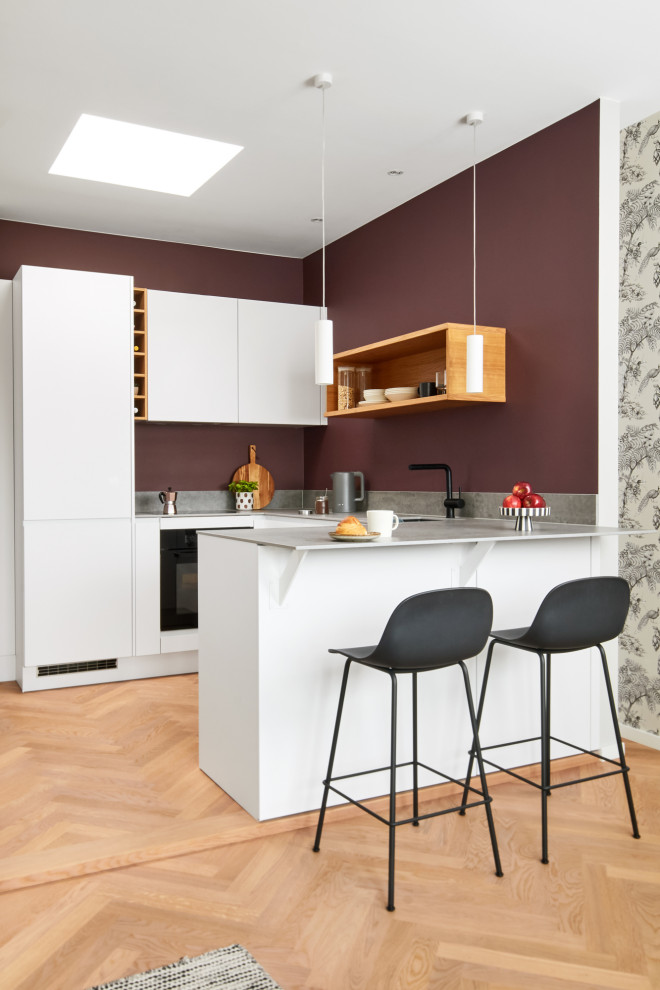 Mid-sized contemporary u-shaped open plan kitchen in Berlin with a drop-in sink, flat-panel cabinets, white cabinets, tile benchtops, red splashback, black appliances, medium hardwood floors, a peninsula and grey benchtop.