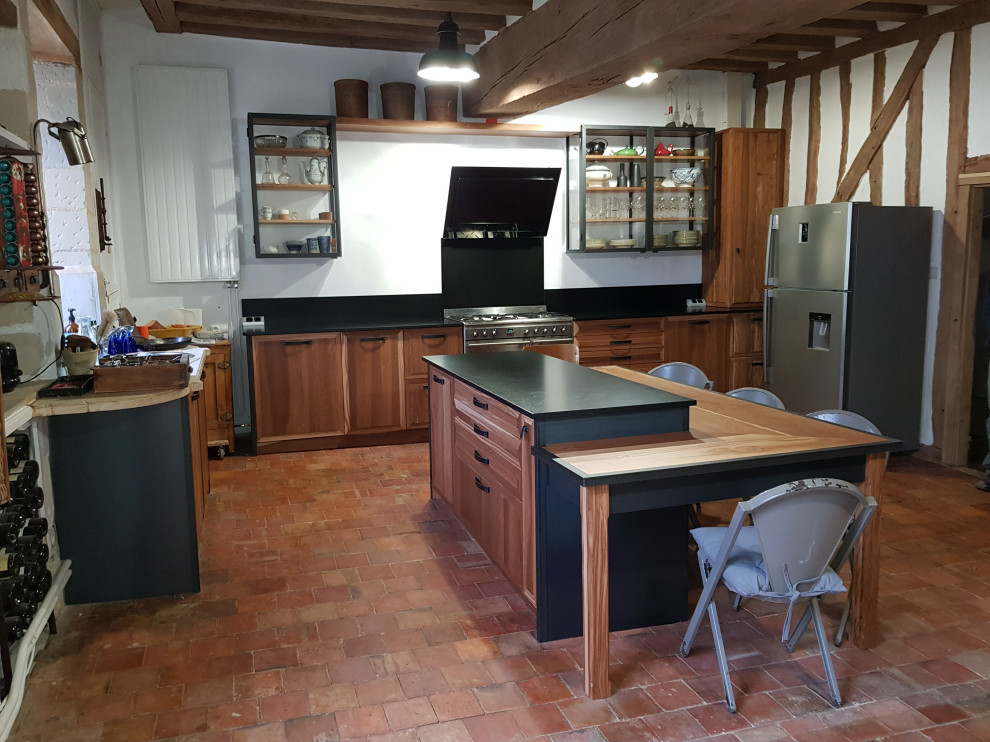 Design ideas for a large industrial open plan kitchen in Angers with an undermount sink, raised-panel cabinets, medium wood cabinets, granite benchtops, black splashback, granite splashback, black appliances, terra-cotta floors, with island, orange floor, black benchtop and exposed beam.