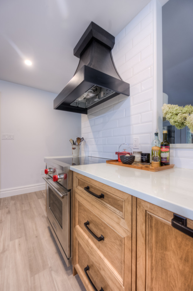 Transitional l-shaped kitchen photo in Toronto with an undermount sink, shaker cabinets, light wood cabinets, white backsplash, stainless steel appliances, an island and white countertops