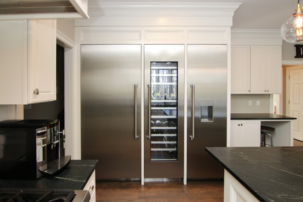 This is an example of a large contemporary u-shaped eat-in kitchen in Boston with an undermount sink, shaker cabinets, white cabinets, granite benchtops, white splashback, subway tile splashback, stainless steel appliances, medium hardwood floors, with island, brown floor and black benchtop.